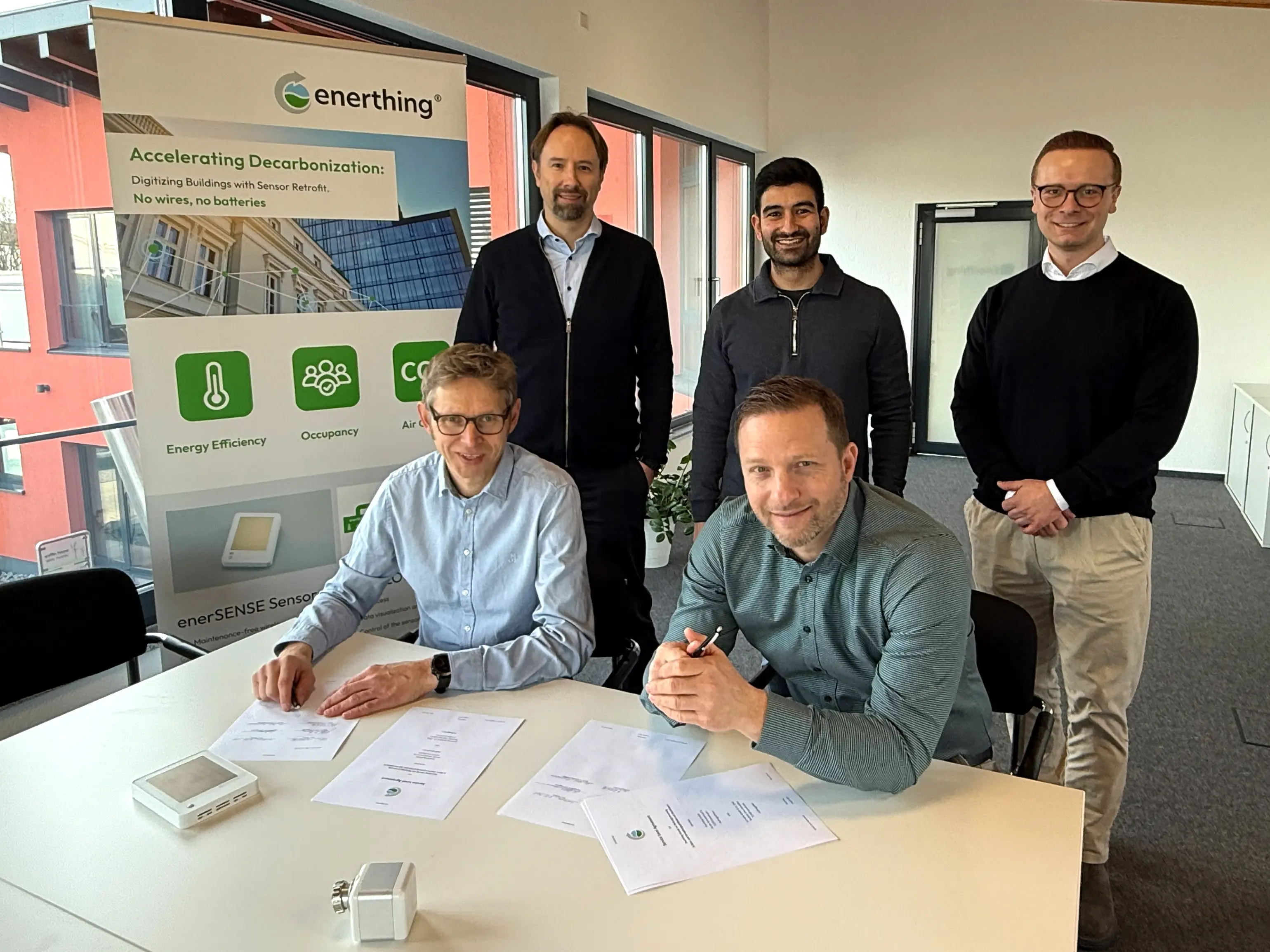 Vertreter von enerthing GmbH und Currenta Conneqtive unterzeichnen die neue Partnerschaft zur Digitalisierung von Bestandsgebäuden. Am Tisch (v. l.): Michael Niggemann und Michael Franz, dahinter Christian Haase, Murat Mutlu und Konstantin Fonk.